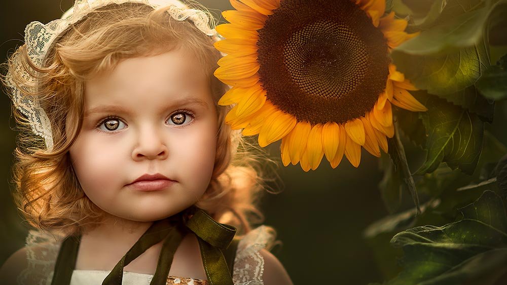 Portrait of a girl with curly hair and a bonnet next to a sunflower.