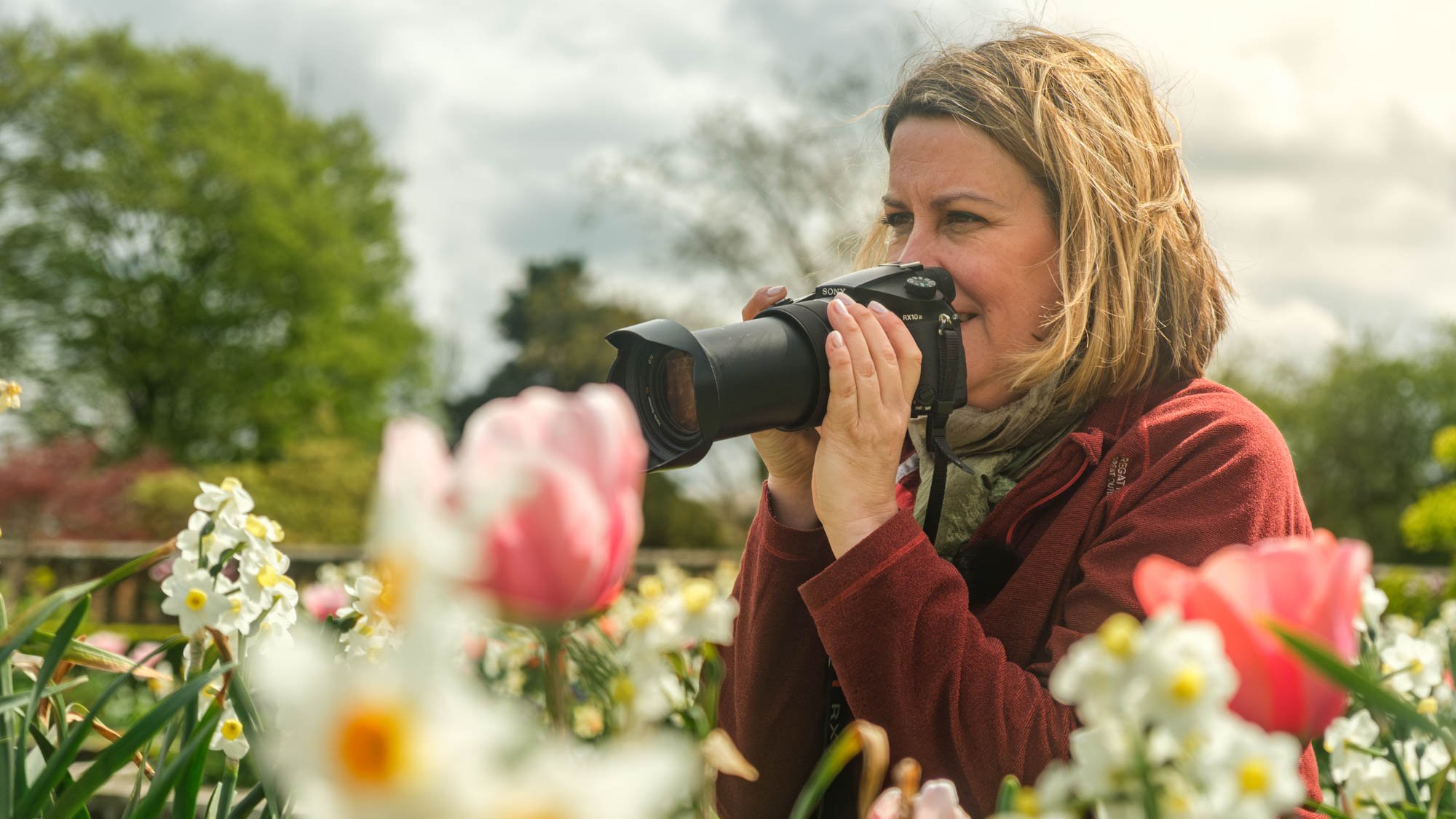 Photographer capturing spring flowers with a Sony camera in a garden filled with tulips and daffodils