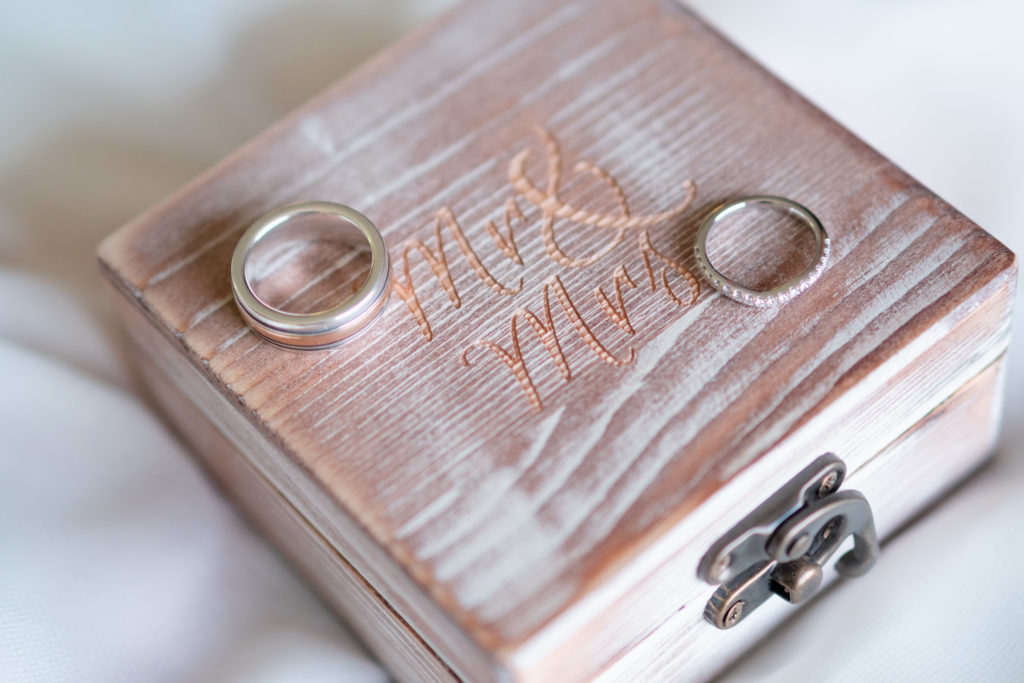 Square wooden ring box with Mr & Mrs inscribed on it with two wedding rings sitting on top.