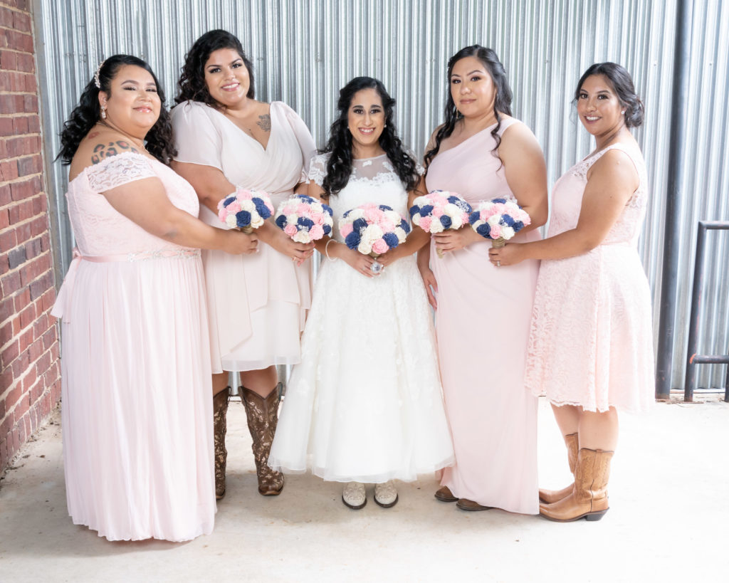 Latino bride with her 4 bridesmaids in light pink dresses around her, all wearing cowboy boots.