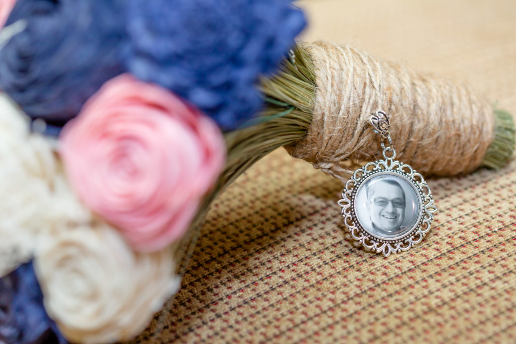 Wedding bouquet with pink, white, & blue flowers with a charm with a man's face.