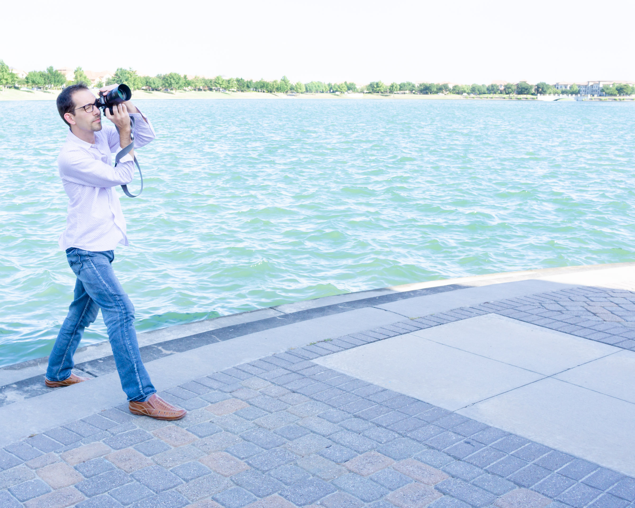 Male Photographer taking a picture right in front of blue water. Selecting your Photographer.